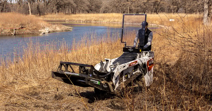 stand-on skid steer brush cutter next to a river